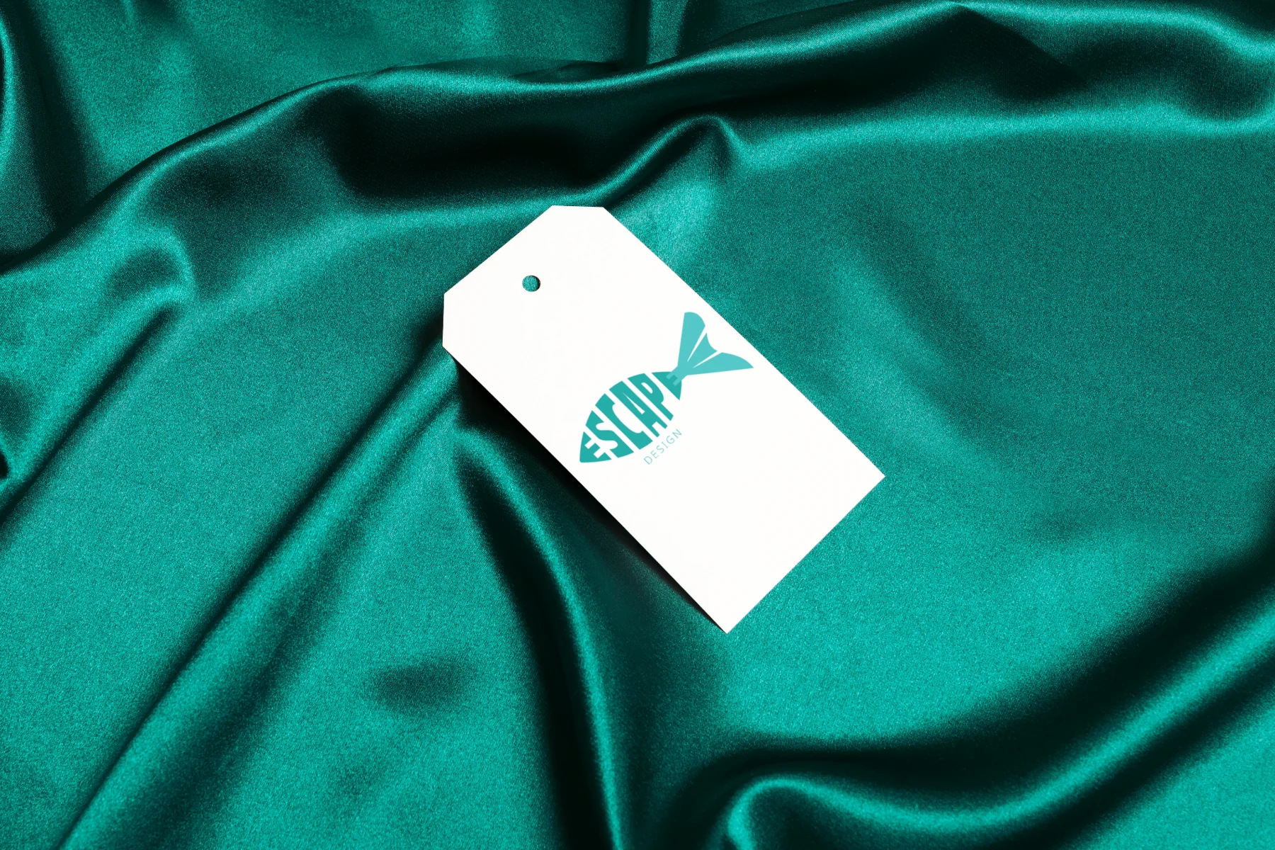Escape Design clothing swing tag placed on teal fabric
