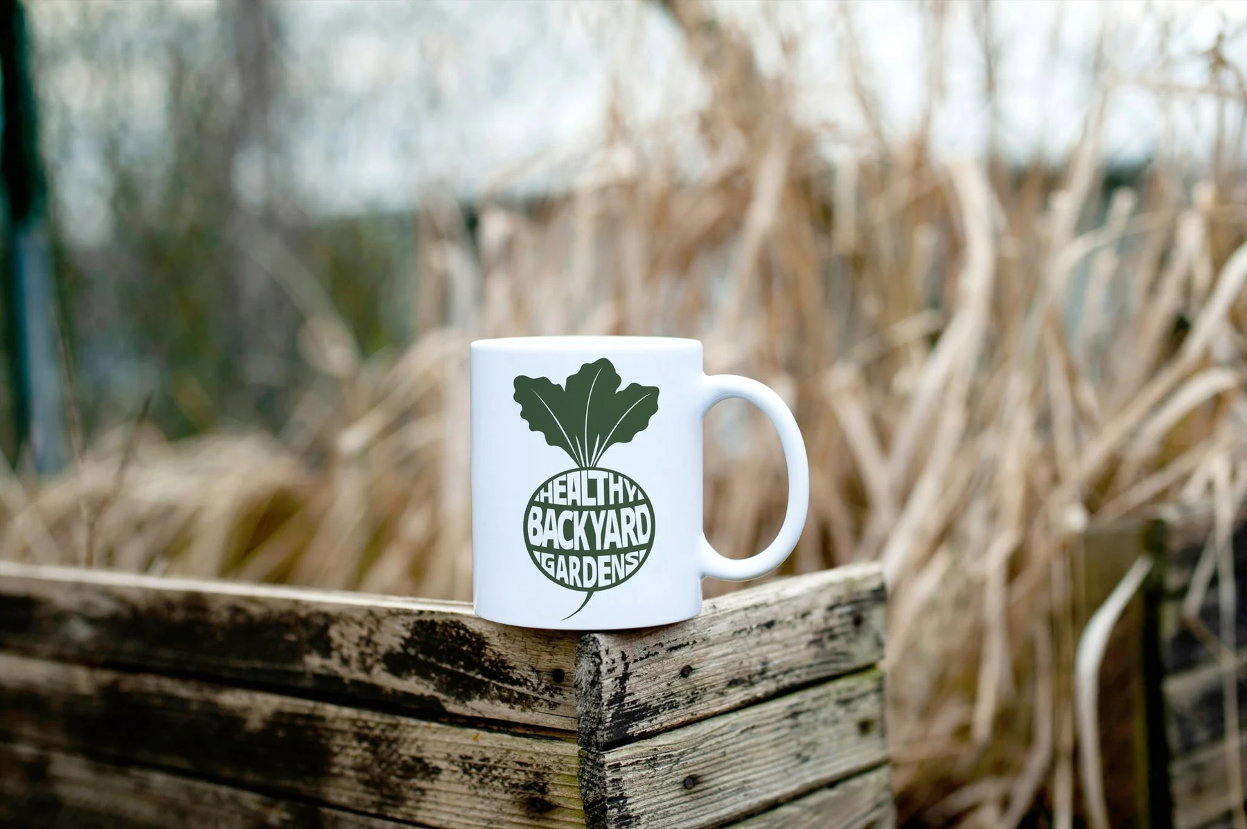 Healthy Backyard Gardens logo on a white mug in a garden setting